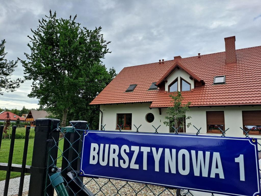 un cartello blu su una recinzione di fronte a una casa di Bursztynowa 1 a Sztutowo