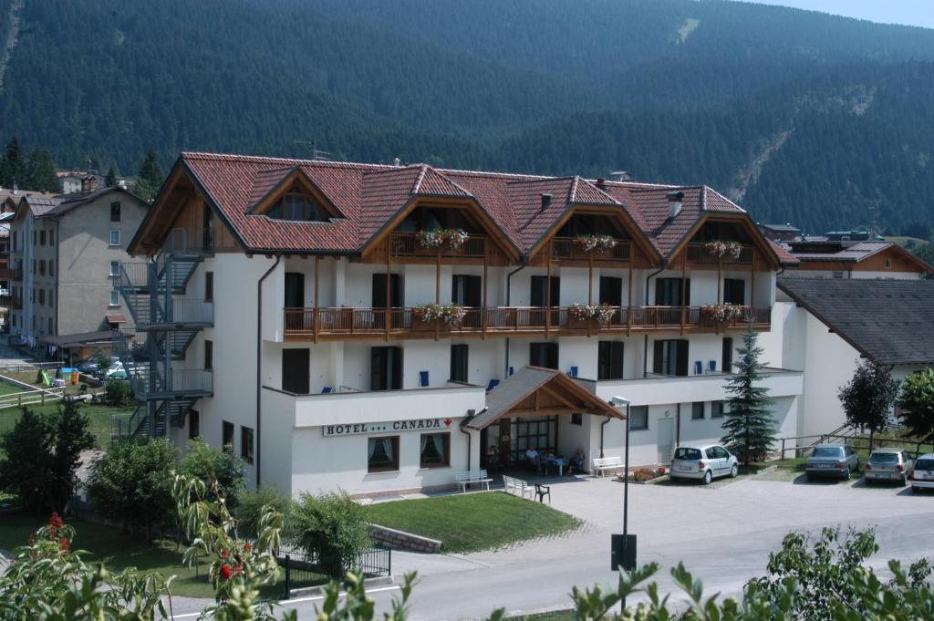 a large white building with a mountain in the background at Hotel Canada in Andalo