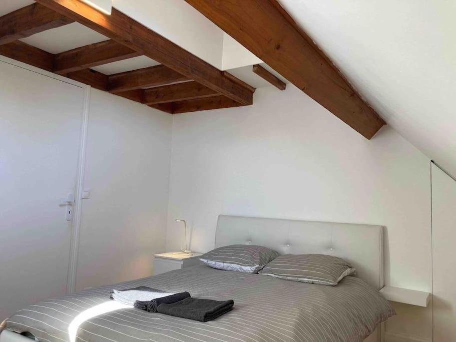 a bed in a white room with a wooden ceiling at Appartement duplex : Le Cosy in Montgeron