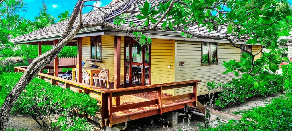 une maison jaune avec une grande terrasse en bois dans l'établissement MOOREA - The Golden Reef Bungalow Nuku Hiva, à Temae