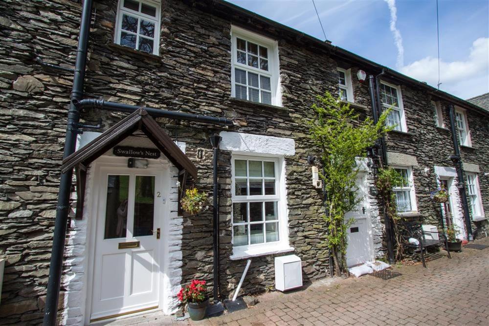 a stone building with a white door and windows at Swallow's Nest in Bowness-on-Windermere