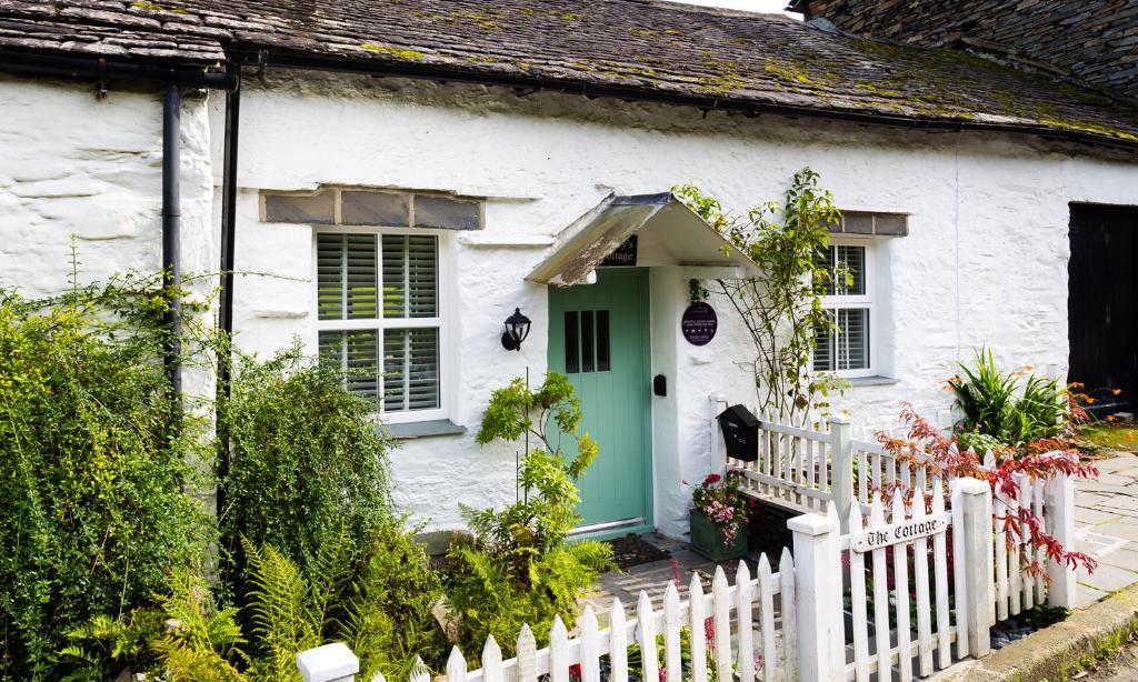 a white house with a green door and a fence at Pennys Cottage in Troutbeck