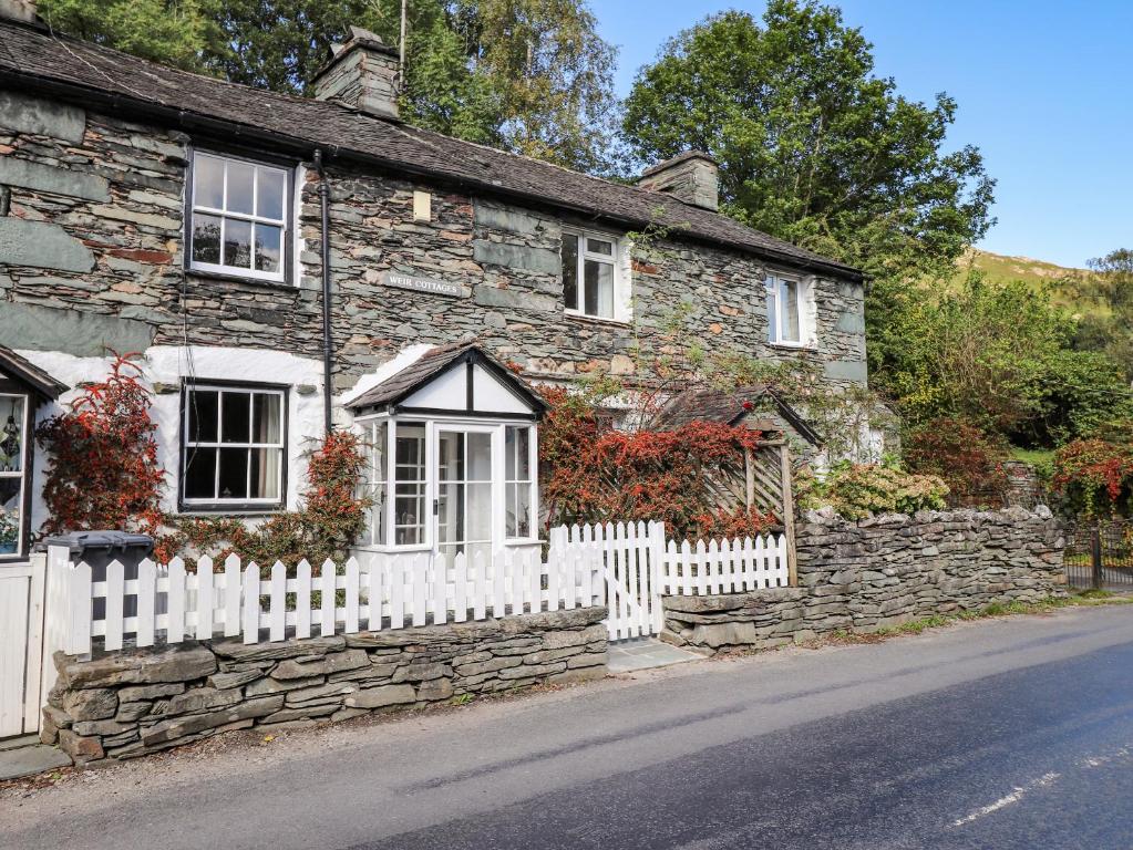 an old stone house with a white fence at Weir Cottage in Ambleside