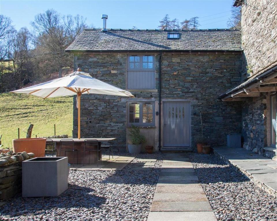 a stone house with an umbrella and a table at Sunny Brow Barn in Ambleside