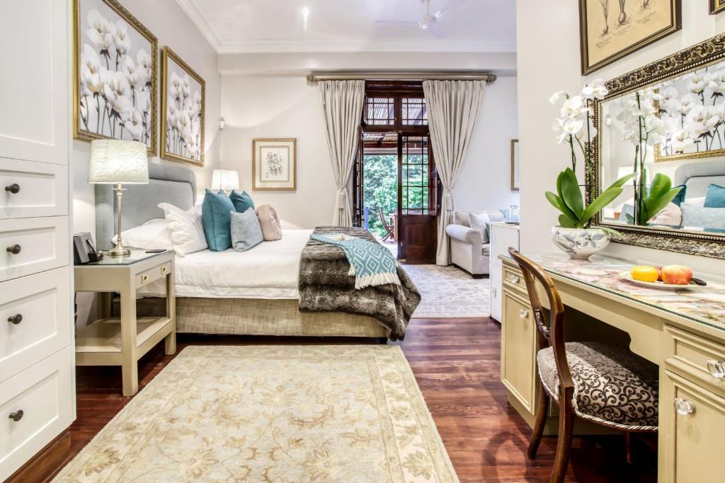 een slaapkamer met een bed en een bureau met een spiegel bij Vredenburg Manor House in Somerset West