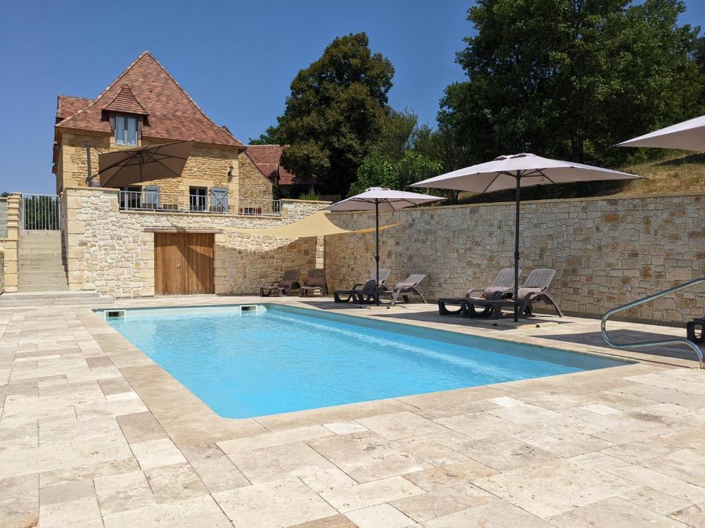 a swimming pool with two umbrellas and a building at Gite de Fleurie - Tursac in Tursac