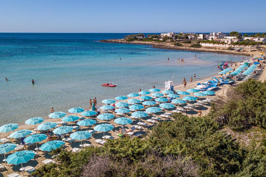 una spiaggia con ombrelloni blu e persone in acqua di PORTO CESAREO CAMPING & Village a Porto Cesareo