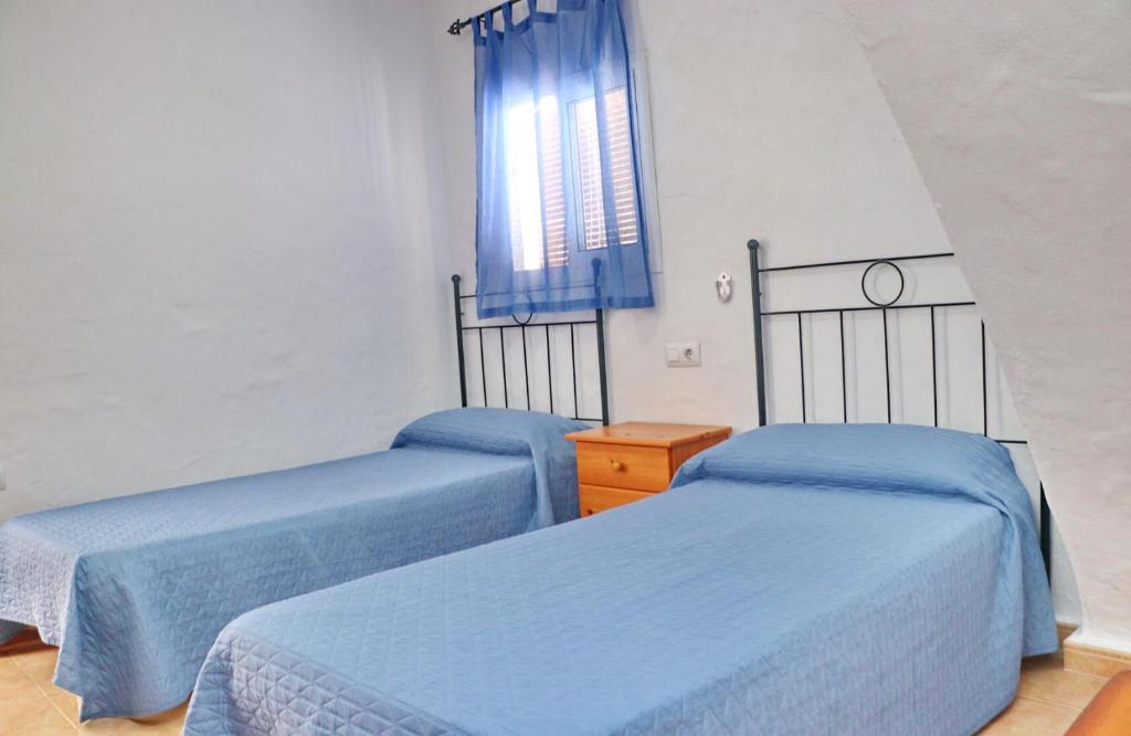 dwa łóżka w pokoju z niebieską pościelą i oknem w obiekcie Apartamento Velarde II w mieście Conil de la Frontera