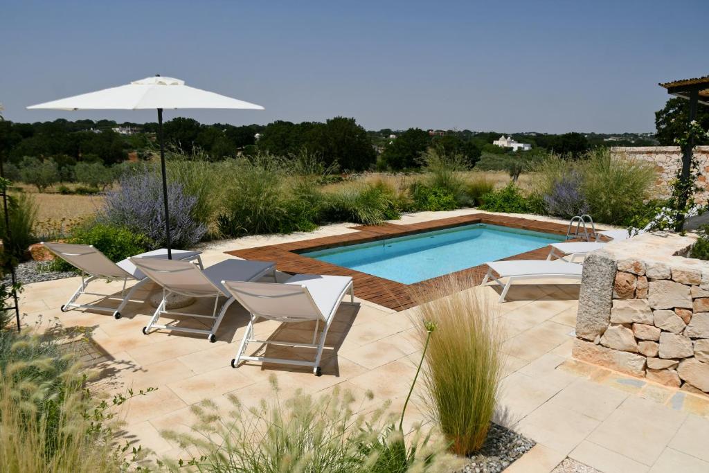 a patio with a pool and chairs and an umbrella at Trulli di Mezza in Cisternino