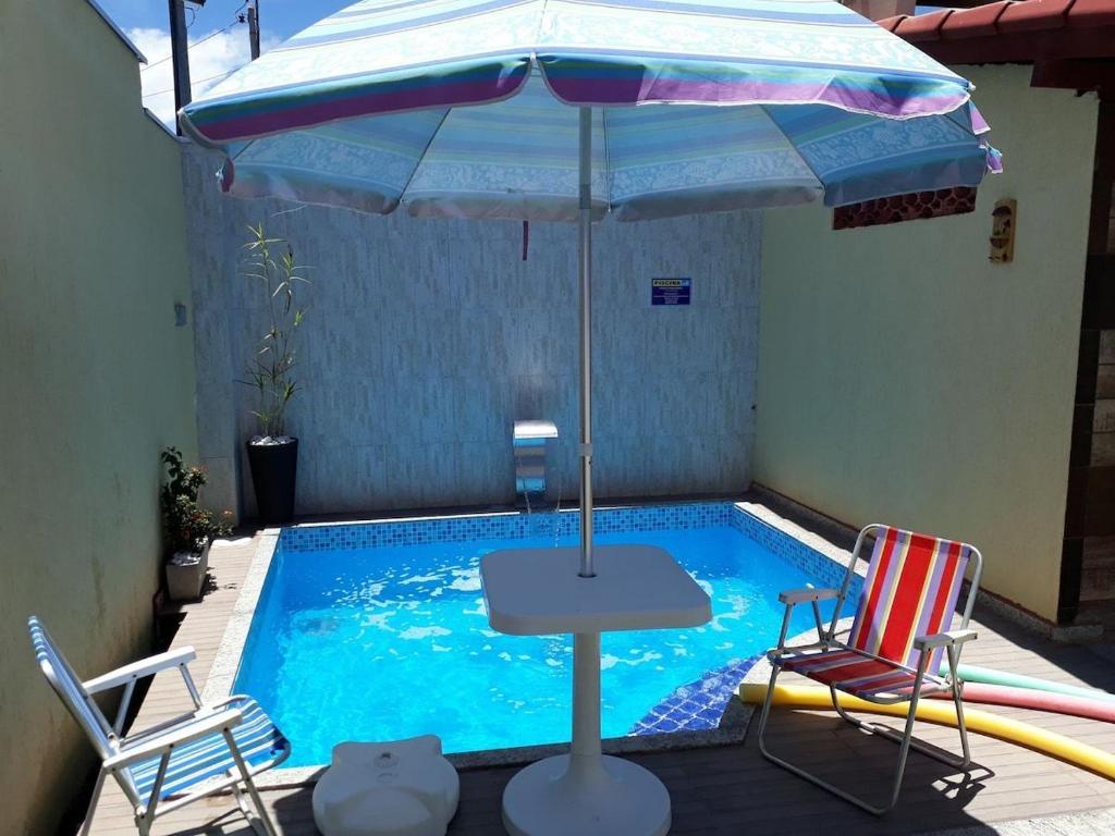 a table with an umbrella next to a swimming pool at Casa Costa das Baleias - Alcobaça,Ba in Alcobaça