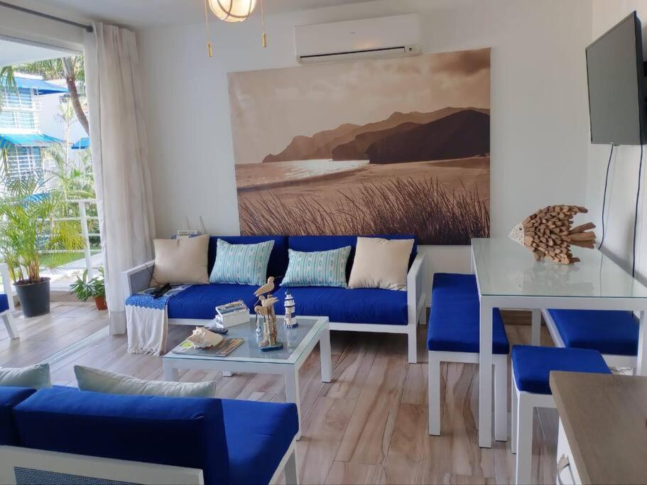 a living room with a blue couch and a table at Juan Dolio-2da Línea de Playa-Acceso Privado-Piscina-Área de Bbq-Gazebos-Jardines-Balcones-Wifi-Telecable-Netflix-Disney Plus-Campos de Gof-Excursiones-Plazas Comerciales-Minimarket-Restaurantes-Bares-Clubes de Playa in Guayacanes