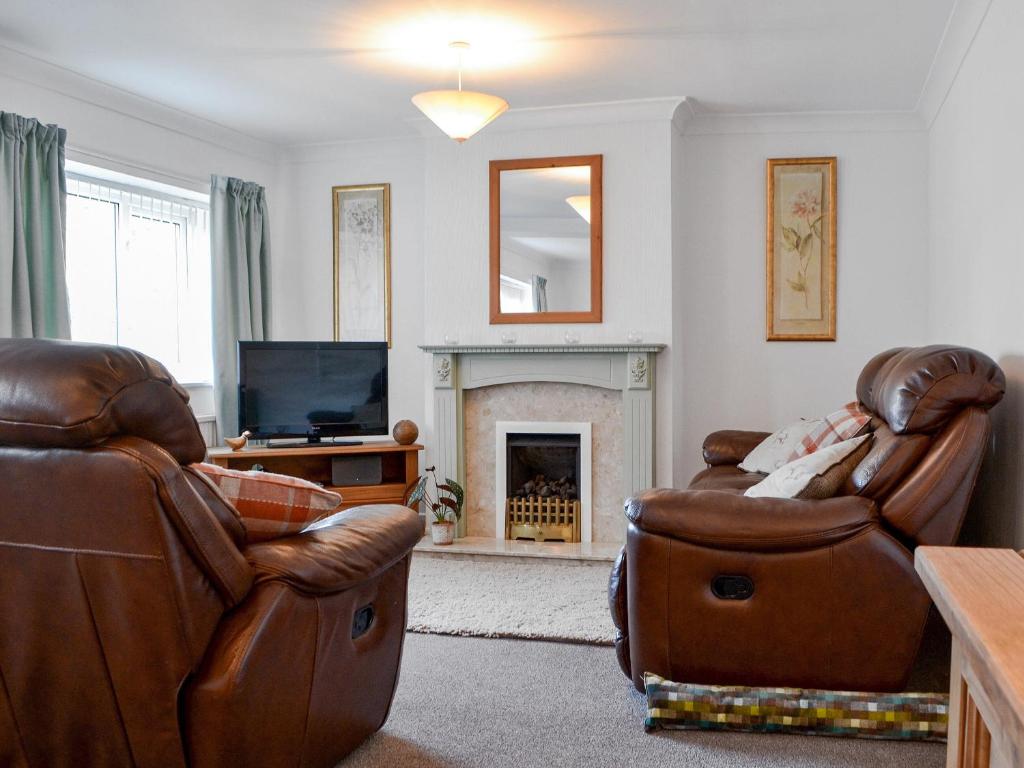a living room with two leather chairs and a fireplace at The Farmhouse At Lane Foot in Tallentire