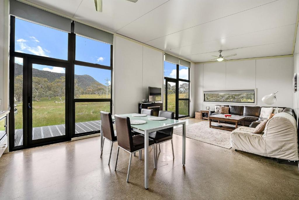 ein Wohnzimmer mit einem Tisch, Stühlen und Fenstern in der Unterkunft Ecocrackenback 7 Sustainable chalet close to the slopes in Crackenback