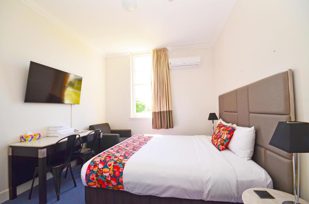 Habitación de hotel con cama, escritorio y TV. en The Hallows Accommodation en Bathurst