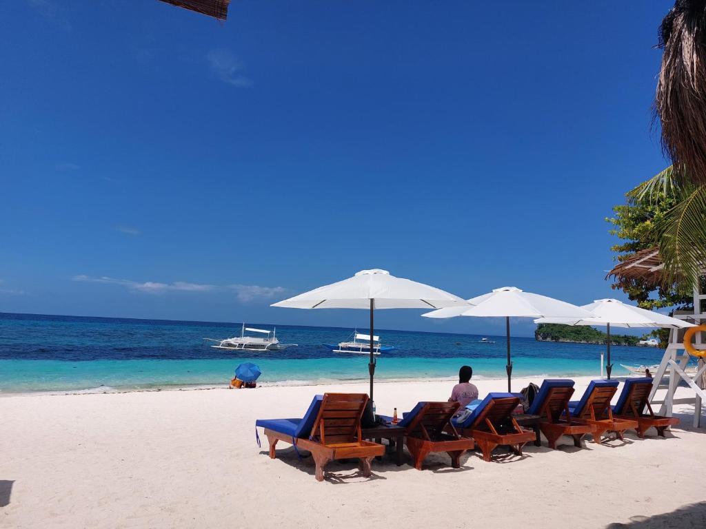 a man sitting on a beach with chairs and umbrellas at Avila's Horizon Dive Resort Malapascua in Malapascua Island