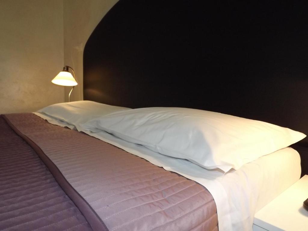 Cama con sábanas blancas y almohadas junto a una lámpara en Locanda Diana, en Iseo