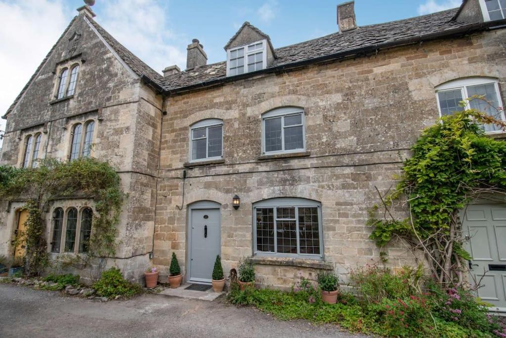 una antigua casa de piedra con una puerta y ventanas blancas en Park Cottage, en Minchinhampton