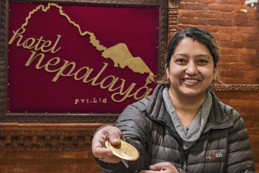 uma mulher segurando uma colher em frente a um sinal revolucionário de hotel em Nepalaya Hotel em Kathmandu