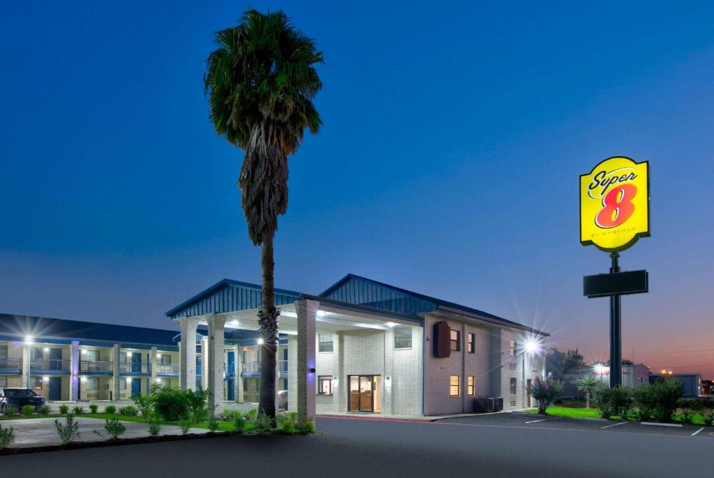 a motel with a palm tree in front of a building at Super 8 by Wyndham Victoria - South - Hwy 59 in Victoria
