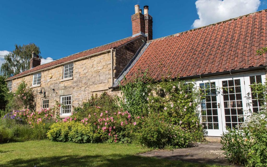 an old stone house with flowers in the yard at Coral Cottage at Castle Howard in York