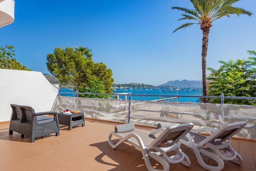 a patio with chairs and a palm tree and the water at Anita Apartments in Port de Pollensa