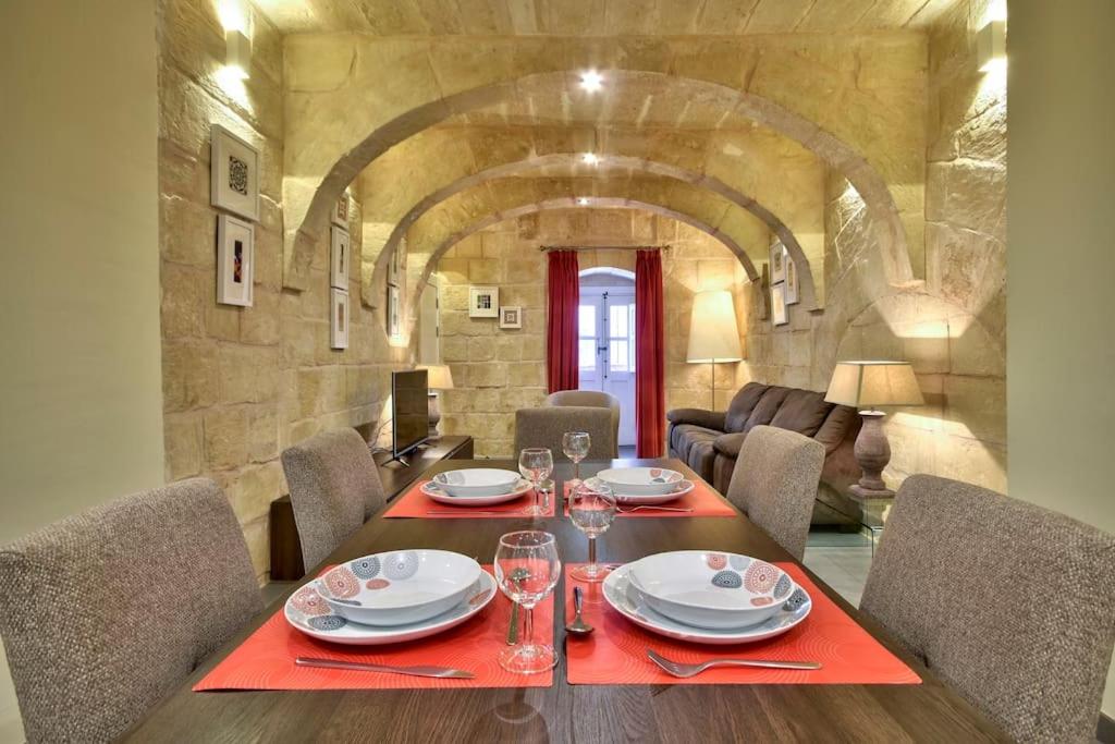 uma sala de jantar com mesa e cadeiras e uma parede de pedra em VALLETTASTAY - ORANGERIE TWO BEDROOM APARTMENT 201 em Valletta