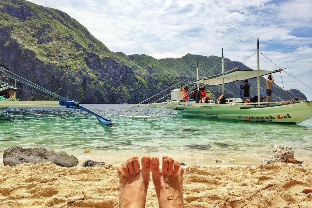 a persons feet in the sand on a beach with a boat at Tribe Banua 