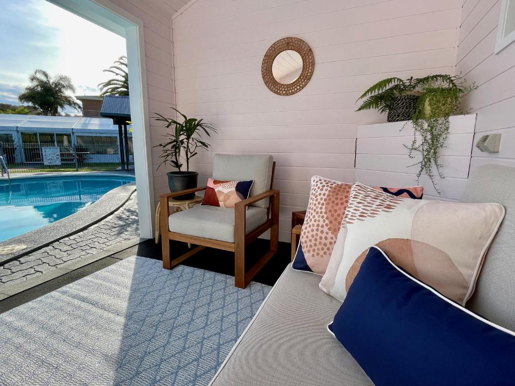 un patio con sofá y una silla junto a la piscina en Pelican Motor Inn, en Merimbula