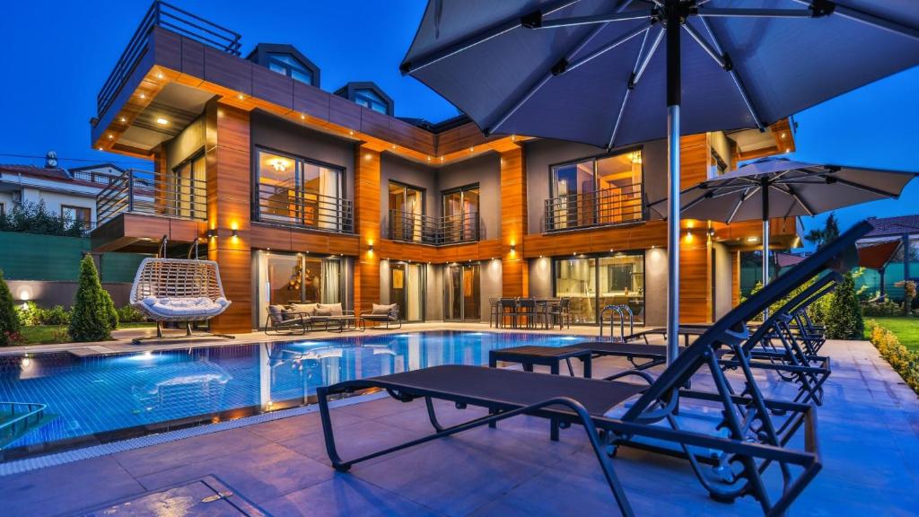a house with a swimming pool with chairs and an umbrella at Luxury Villa Close to Shops and Restaurants -Large Garden Pool Table and Table Tennis in Fethiye