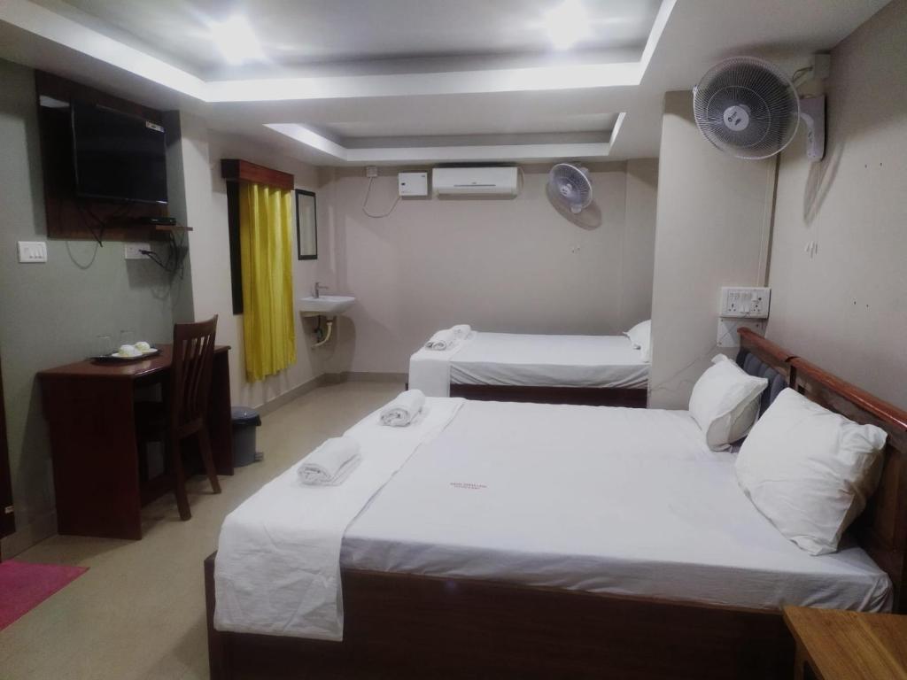 a room with two beds and a desk and a television at HOTEL COSTA LAND in Port Blair