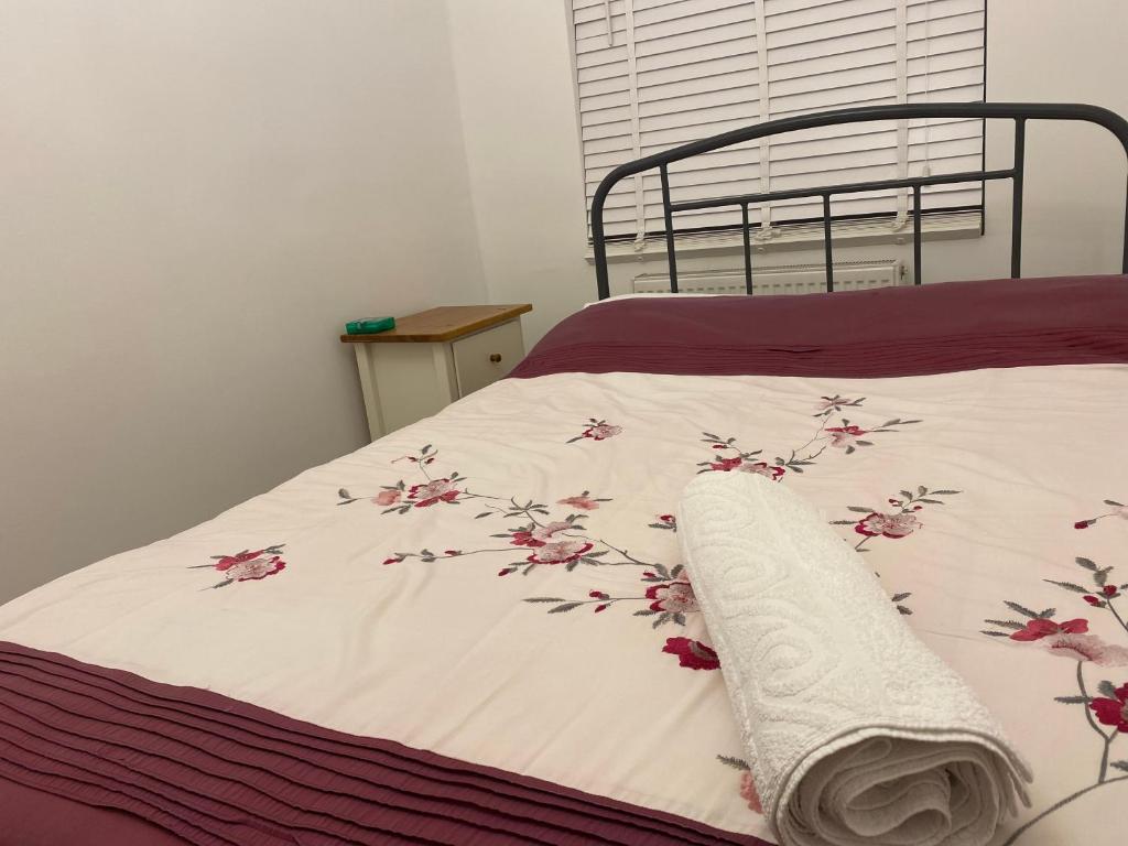 a bed with a white blanket with pink flowers on it at London Rooms with Free Parking 134 in Stone Grove
