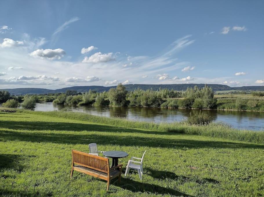 una mesa y dos sillas y un banco junto a un río en Schöne Wohnung, direkt an der Weser, mit Kaminofen, en Hessisch Oldendorf