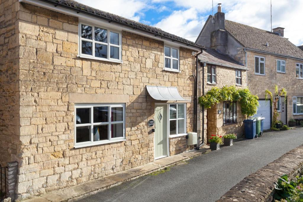 a stone house with white windows on a street at Forge Cottage in Winchcombe