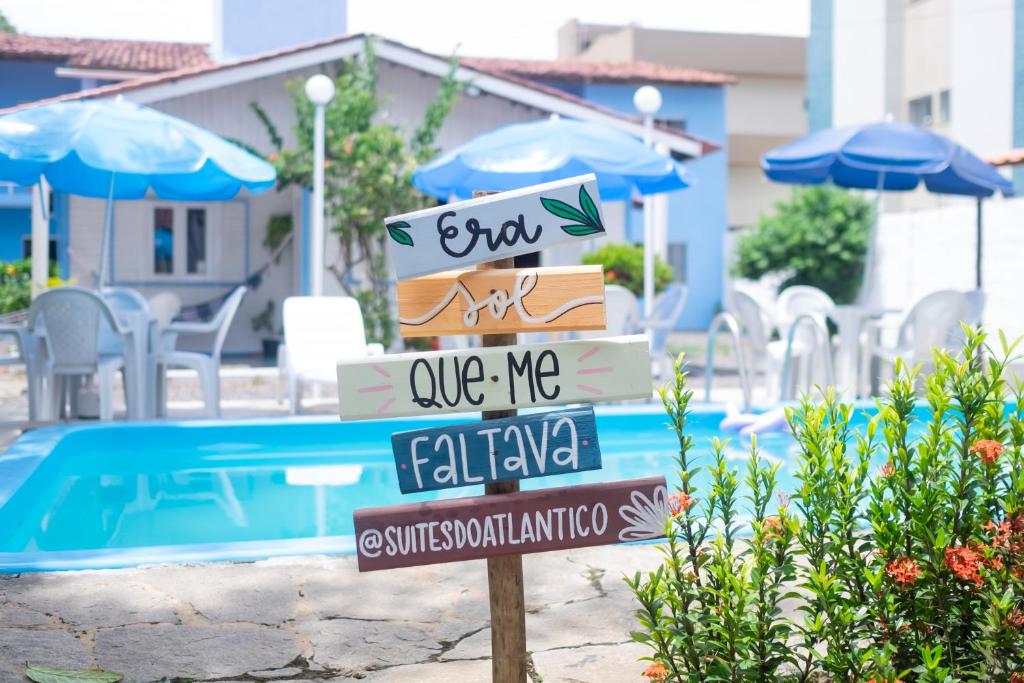 a sign in front of a swimming pool with umbrellas at Pousada Suítes do Atlântico in Ilhéus