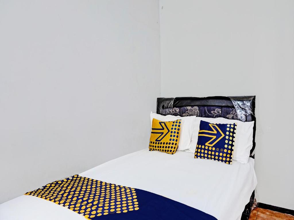 a white bed with yellow and blue pillows on it at SPOT ON 1711 Serayu Sumbersari Residence in Malang