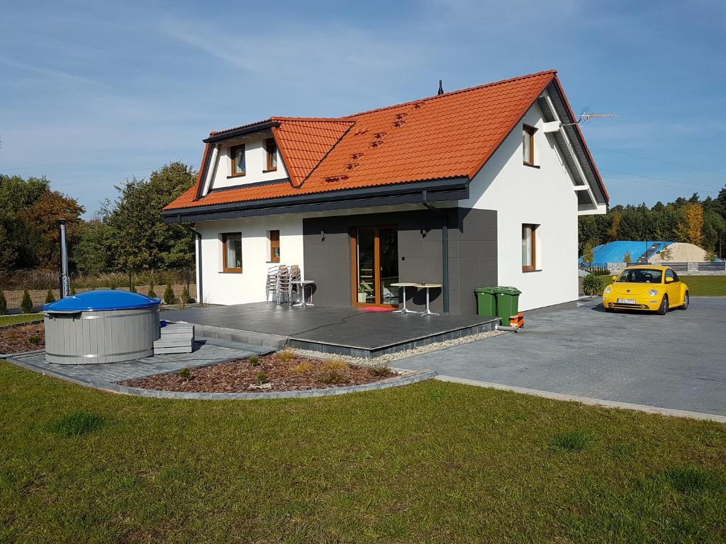 ein weißes Haus mit einem orangenen Dach und einem gelben Auto in der Unterkunft Domki u Stefana in Józefów