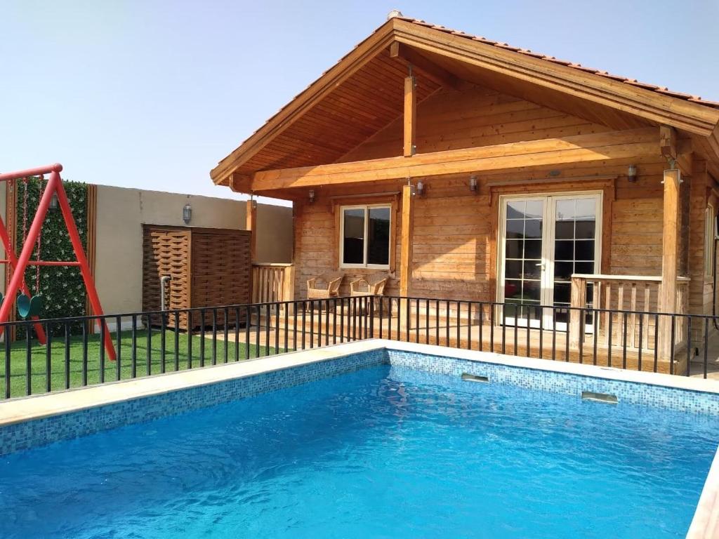 una casa con piscina frente a una casa en شاليهات الكوخ السويسري وأكوابارك, en Ash Shishah