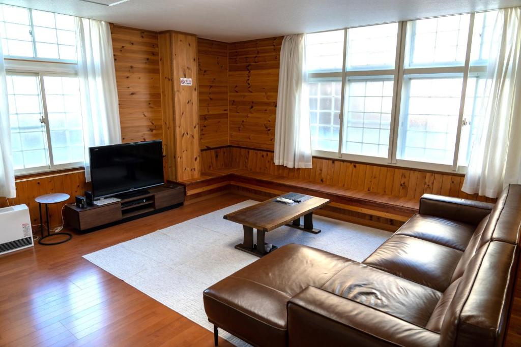 un soggiorno con divano in pelle e TV di Asagama House a Nozawa Onsen