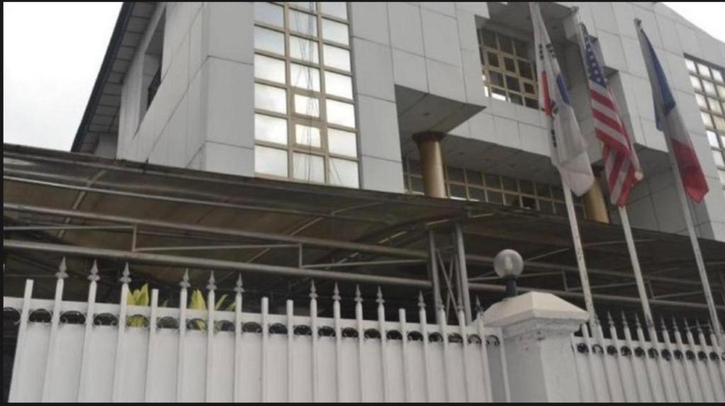 a white fence in front of a building with flags at Whitehouse Msquare Hotel in Ikeja