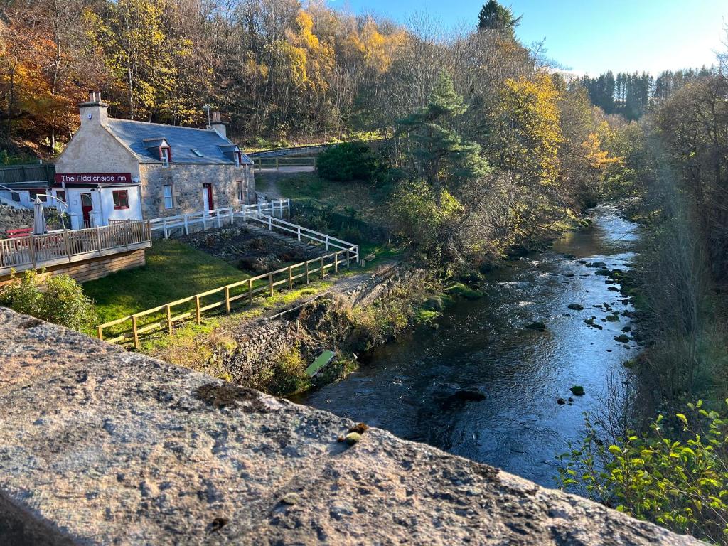 an old building next to a river with trees at The Fiddichside Inn in Aberlour