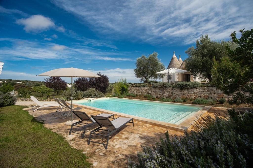 a pool with chairs and an umbrella and a house at Country House da Già in Ostuni