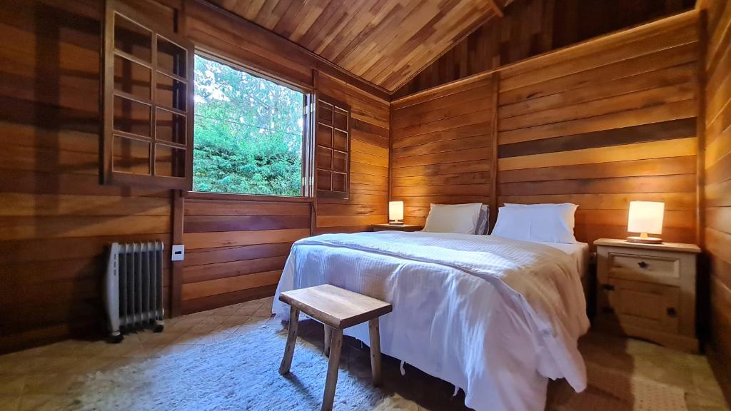 a bedroom with a bed with wooden walls and a window at Chalé Arado 313 in Monte Verde