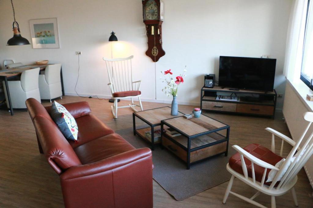uma sala de estar com um sofá e cadeiras e uma televisão em Duinroos em Nes