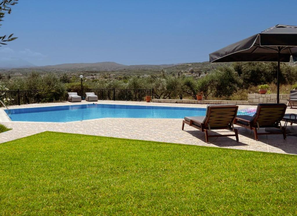 a swimming pool with two chairs and an umbrella at Villas Lefkothea with Large Pool, Playground Area, & Magnificent Views! in Adelianos Kampos