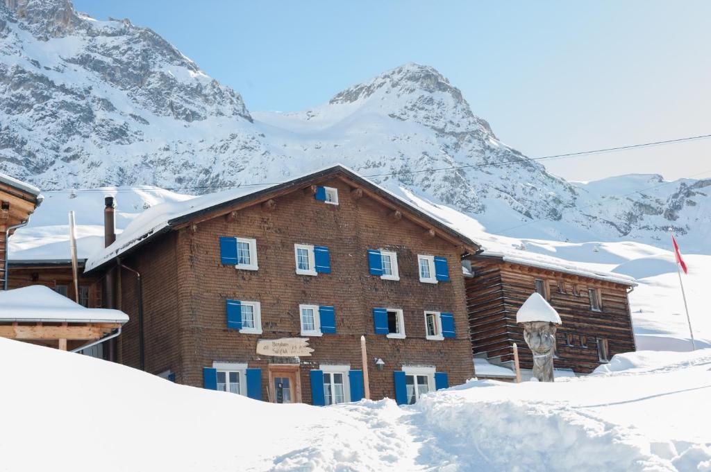 un edificio en la nieve con una montaña en el fondo en Berghaus Sulzfluh en Sankt Antönien