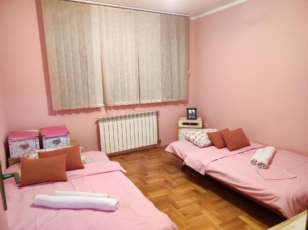 two beds in a room with pink walls and wooden floors at Stan na dan Pale Apartman Danica in Pale