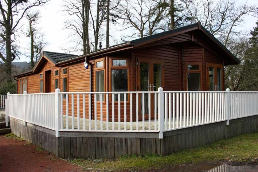 a small wooden cabin with a white fence at Loch Lomond Sanctuary Lodges in Balloch