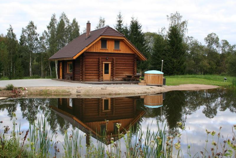 une cabane en rondins avec sa réflexion dans un corps d'eau dans l'établissement Vana-Laane Puhkemaja, à Otepää
