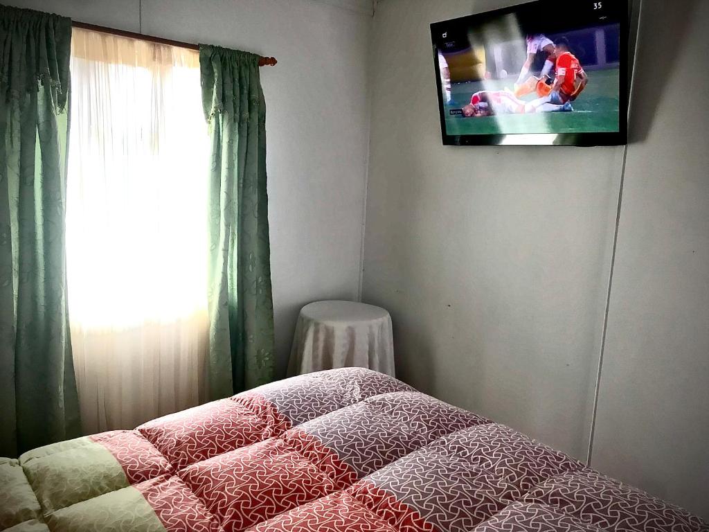 - une chambre avec un lit et une télévision murale dans l'établissement Cabañas Esmeralda con Desayuno Continental, à Punta Arenas