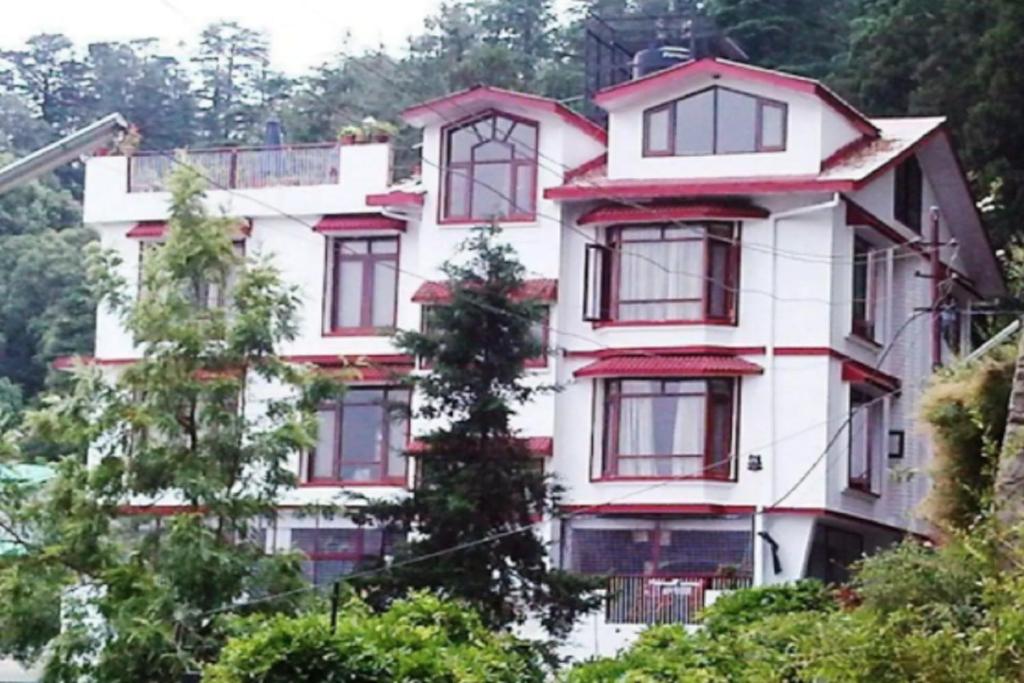 a white building with red windows and trees at Goroomgo Marc Shimla Near Mall Road - Luxury Room - Excellent Service - Ample Parking - Best Hotel in Shimla in Shimla
